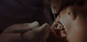 Dentist examining a patients teeth in the dentists chair under bright light at the dental clinic;