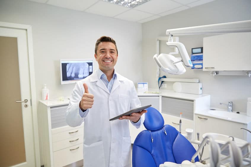 people, medicine, stomatology and healthcare concept - happy middle aged male dentist in white coat with tablet pc computer showing thumbs up at dental clinic office