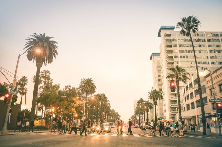 Locals and tourists walking on zebra crossing and on Ocean Ave in Santa Monica after sunset - Crowded streets of Los Angeles and California state - Warm desat twilight color tones with blurred people